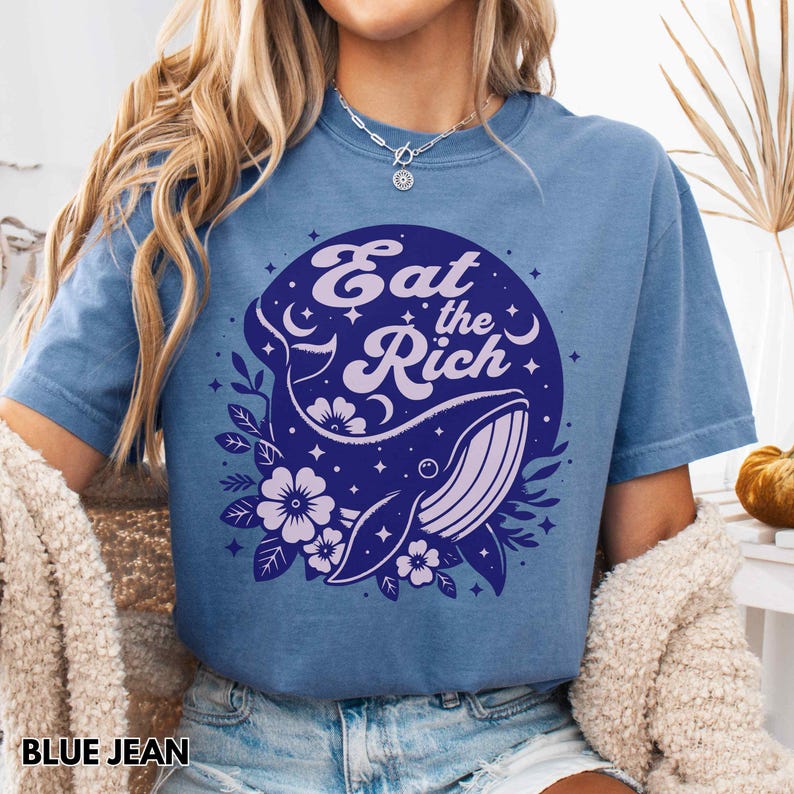 May include: A blue jean t-shirt featuring a whale and floral graphic. The graphic reads "Eat the Rich" in a retro font.