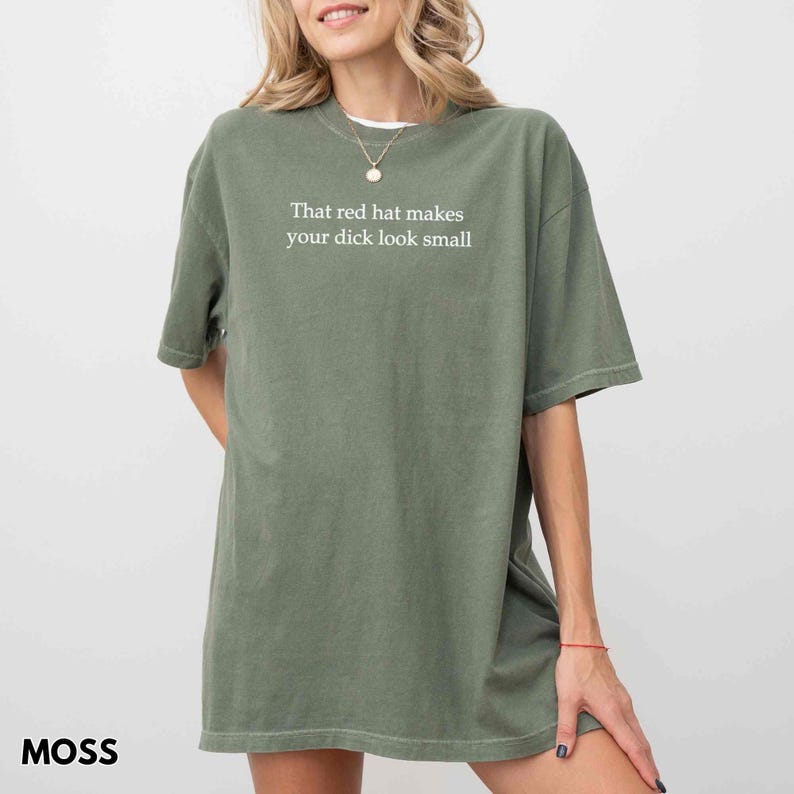 Może przedstawiać: Zielona koszulka w kolorze mchu z białym napisem: "That red hat makes your dick look small". Koszulka ma luźny kr&oacute;j i kr&oacute;tkie rękawy. Słowo "MOSS" jest wydrukowane w lewym dolnym rogu.