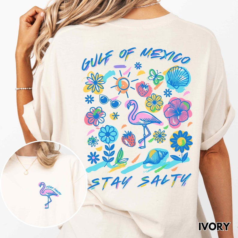 May include: A white t-shirt with a colorful graphic design featuring a flamingo, flowers, a seashell, sunglasses, and the text "Gulf of Mexico Stay Salty".