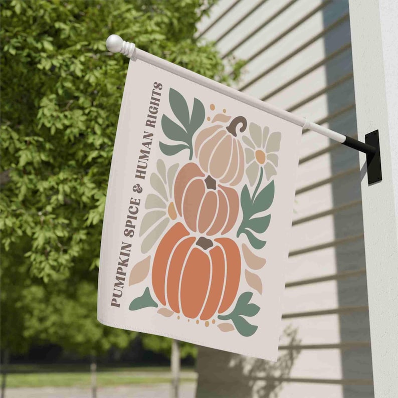 May include: A cream-colored outdoor flag featuring a stacked pumpkin design in shades of orange, brown, and beige, with green leaves and white flowers. The text "PUMPKIN SPICE & HUMAN RIGHTS" is printed vertically on the left side.