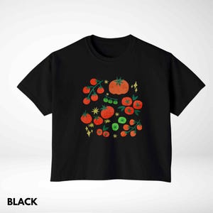 Puede incluir: Camiseta negra con una colorida ilustraci&oacute;n de tomates y ramas de tomate. El dise&ntilde;o incluye tomates rojos de varios tama&ntilde;os, hojas verdes y detalles en forma de estrella amarilla. La palabra "BLACK" est&aacute; impresa en la parte inferior.