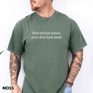Może przedstawiać: Zielona koszulka w kolorze mchu z białym napisem "That red hat makes your dick look small". Koszulka ma okrągły dekolt i kr&oacute;tkie rękawy. Słowo "MOSS" jest wydrukowane w lewym dolnym rogu.
