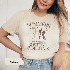 Puede incluir: Una camiseta beige con un dise&ntilde;o gr&aacute;fico marr&oacute;n que dice "Summers are made for Bostons & Bellinis". El gr&aacute;fico tambi&eacute;n incluye una imagen de dibujos animados de un perro Boston Terrier y una copa de champ&aacute;n.