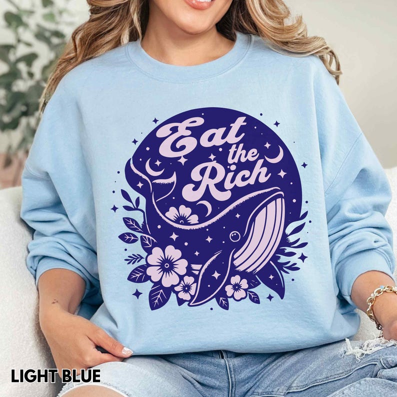 May include: Light blue sweatshirt featuring a whale graphic with stars and the text "Eat the Rich" in a circle.