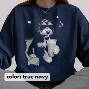 K&ouml;nnte beinhalten: Ein marineblaues Sweatshirt mit einer Grafik eines Hundes, der eine Sonnenbrille tr&auml;gt und aus einem Becher mit Strohhalm trinkt. Der Text "color: true navy" steht unten. Der Hund ist schwarz und wei&szlig;, und das Getr&auml;nk scheint Eiskaffee zu sein.