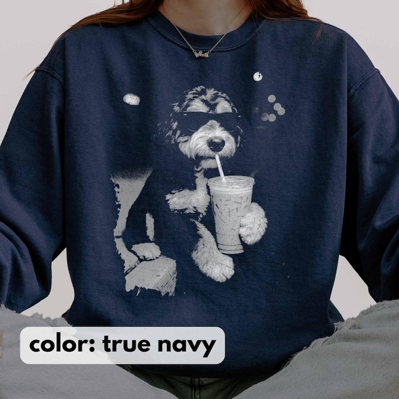 K&ouml;nnte beinhalten: Ein marineblaues Sweatshirt mit einer Grafik eines Hundes, der eine Sonnenbrille tr&auml;gt und aus einem Becher mit Strohhalm trinkt. Der Text "color: true navy" steht unten. Der Hund ist schwarz und wei&szlig;, und das Getr&auml;nk scheint Eiskaffee zu sein.