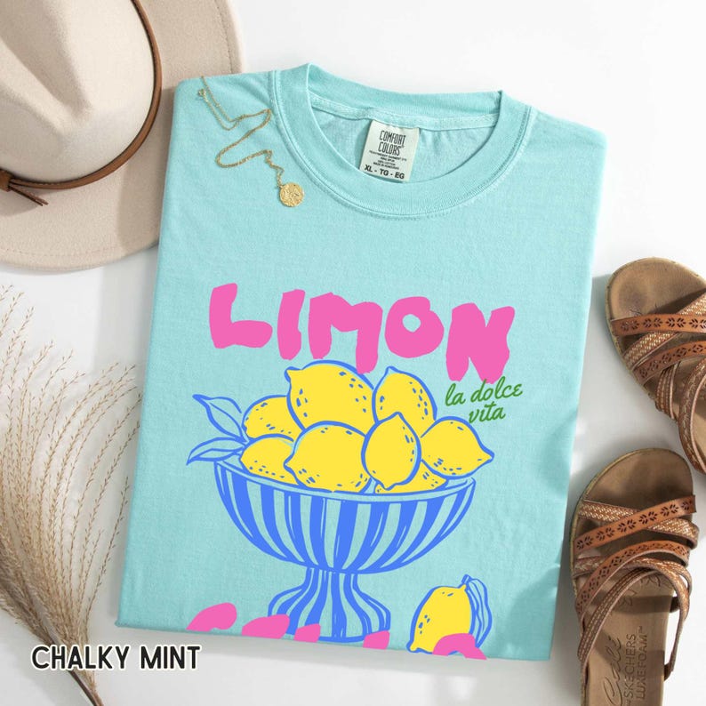 May include: A light blue t-shirt with the word "LIMON" in pink, and a graphic of lemons in a blue bowl. The text "la dolce vita" is below the word "LIMON". The shirt is labeled "CHALKY MINT" and is size XL-TO-80.