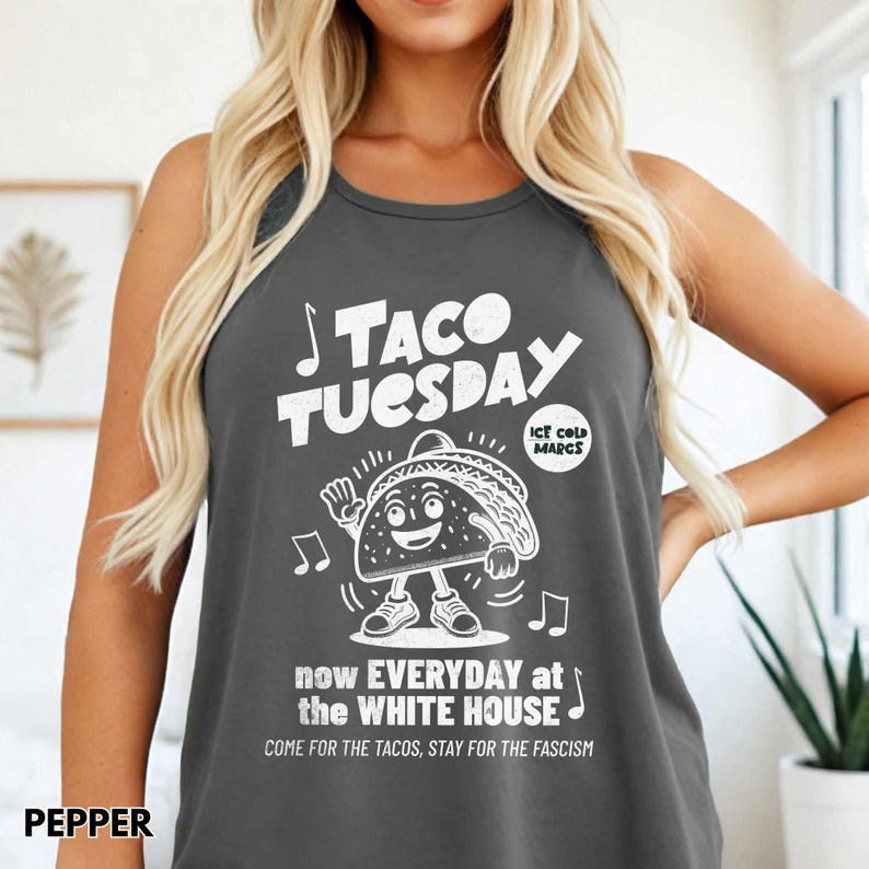 May include: Dark gray tank top with the words "TACO TUESDAY" in white, along with a cartoon taco character. The text "now EVERYDAY at the WHITE HOUSE" and "COME FOR THE TACOS, STAY FOR THE FASCISM" are also printed on the shirt.