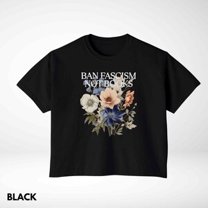 Puede incluir: Camiseta negra con un dise&ntilde;o floral y el texto "BAN FASCISM NOT BOOKS" en blanco. El arreglo floral incluye flores blancas, rosas y azules. La camiseta es de cuello redondo.