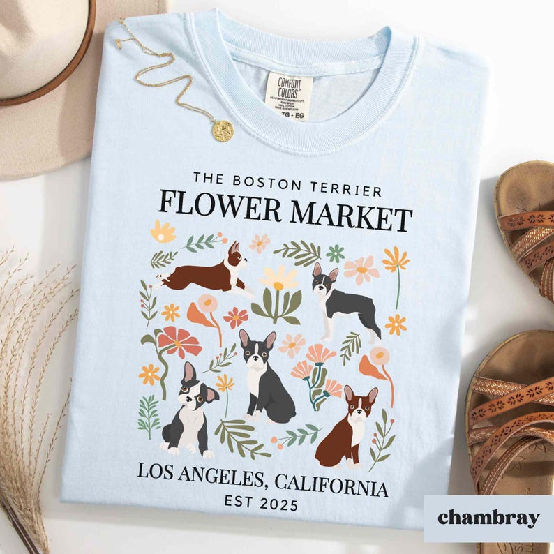 May include: Light blue t-shirt with a floral design featuring Boston Terriers. The text "The Boston Terrier Flower Market Los Angeles, California Est 2025" is printed on the shirt.