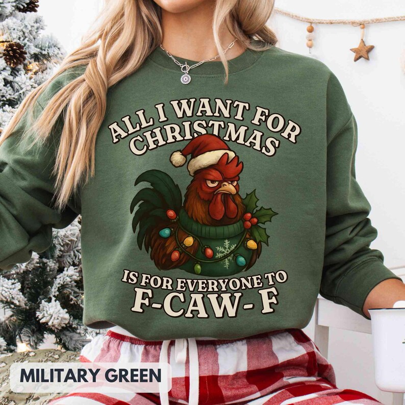 May include: Military green sweatshirt with a Christmas rooster graphic. The text reads "ALL I WANT FOR CHRISTMAS IS FOR EVERYONE TO F-CAW-F". The rooster wears a Santa hat and a sweater with Christmas lights.