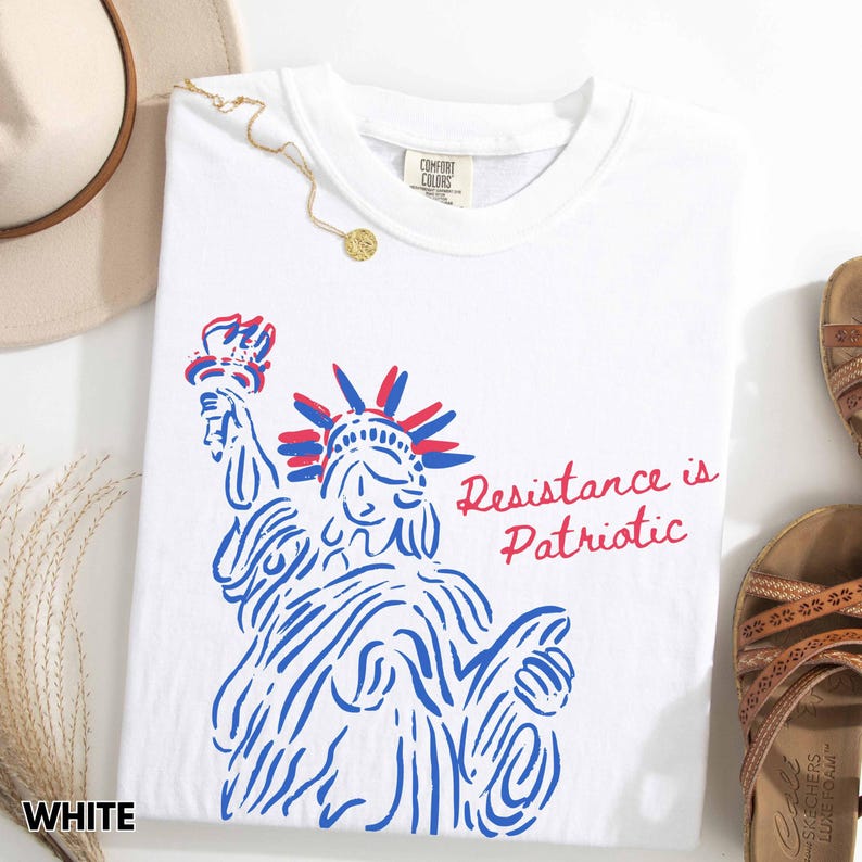 Pu&ograve; includere: T-shirt bianca con grafica blu e rossa della Statua della Libert&agrave; e la scritta "Resistance is Patriotic". La maglietta ha un girocollo e un'etichetta "Comfort Colors".