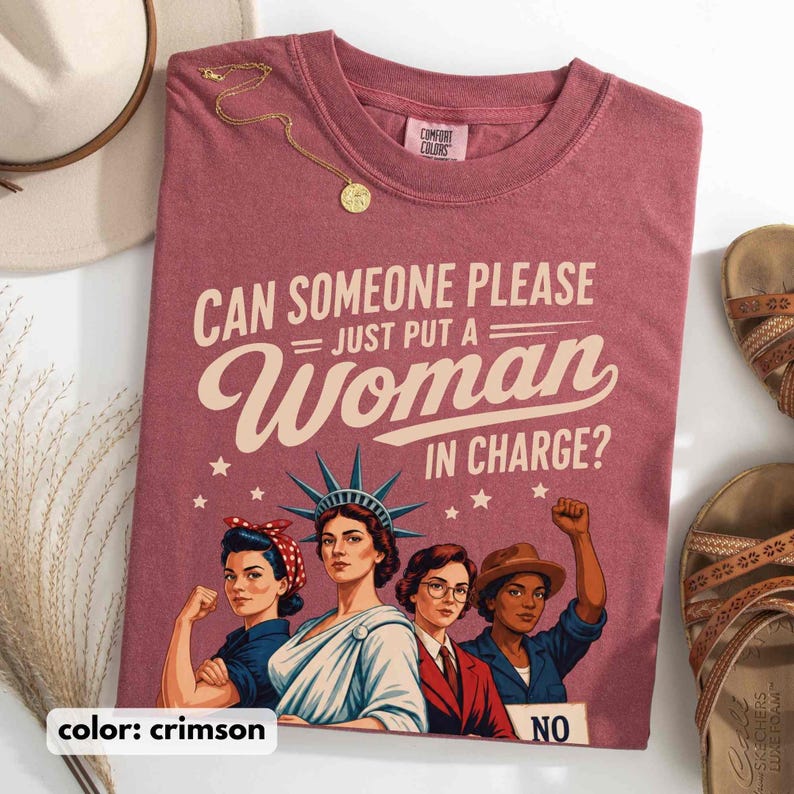 May include: Crimson t-shirt with the text "CAN SOMEONE PLEASE = JUST PUT A Woman IN CHARGE?" and an illustration of four women. A gold necklace and sandals are also visible.
