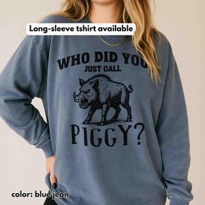 Op de afbeelding: Blauw spijkerbroek sweatshirt met lange mouwen met de tekst "WHO DID YOU JUST CALL PIGGY?" en een afbeelding van een wild zwijn. De tekst "Long-sleeve tshirt available" staat bovenaan.