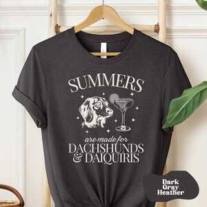 May include: Dark gray heather t-shirt with a white graphic design. The graphic features a dachshund with a martini glass and the text "Summers are made for Dachshunds & Daiquiris".
