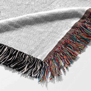 May include: Close-up of the fringe on a woven throw blanket. The fringe is a mix of black, white, blue, red, green, and yellow threads.