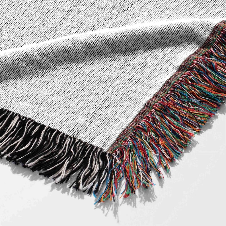 May include: Close-up of the fringe on a woven throw blanket. The fringe is a mix of black, white, blue, red, green, and yellow threads.
