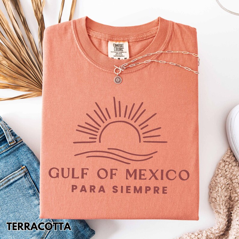 May include: Terracotta t-shirt with a graphic of a sunset over a wave and the text "Gulf of Mexico Para Siempre".