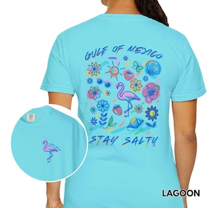 May include: A light blue t-shirt with a graphic print of a flamingo, flowers, and the text "Gulf of Mexico Stay Salty".