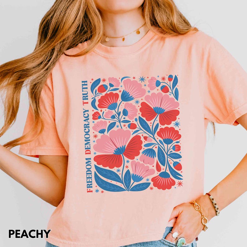 May include: Peach-colored t-shirt with a floral design in red, pink, and blue. The words "FREEDOM DEMOCRACY TRUTH" are printed vertically on the left side. The word "PEACHY" is printed at the bottom.