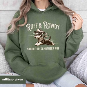 May include: A military green hooded sweatshirt with the text "Ruff & Rowdy Saddle Up, Schnauzer Pup" and a cartoon image of a schnauzer wearing a cowboy hat.