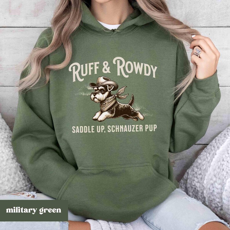 May include: A military green hooded sweatshirt with the text "Ruff & Rowdy Saddle Up, Schnauzer Pup" and a cartoon image of a schnauzer wearing a cowboy hat.
