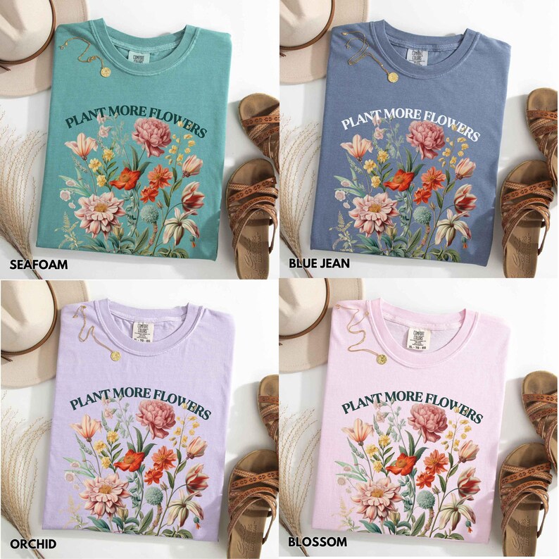 Op de afbeelding: Vier T-shirts in de kleuren zeegroen, spijkerbroekblauw, orchidee en bloesem. Elk shirt heeft de tekst "PLANT MORE FLOWERS" boven een bloemenontwerp met rode, roze en witte bloemen. Accessoires zijn sandalen en een hoed.