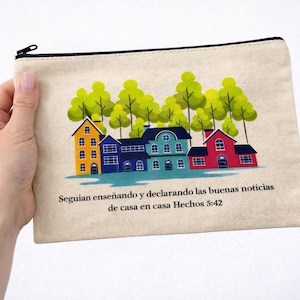 May include: A beige canvas zippered pouch featuring a colorful illustration of houses and trees. The houses are in shades of yellow, blue, and red. Text in Spanish is printed below the houses.