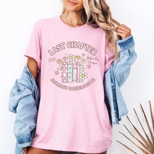 May include: A light pink t-shirt with a graphic design for a bachelorette party. The design includes the text "Last Chapter 2025 before the Chapel" and "Amanda's Bachelorette" with floral and book illustrations.