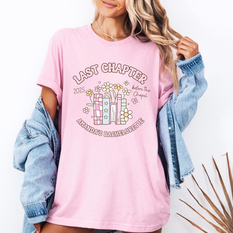 May include: A light pink t-shirt with a graphic design for a bachelorette party. The design includes the text "Last Chapter 2025 before the Chapel" and "Amanda's Bachelorette" with floral and book illustrations.