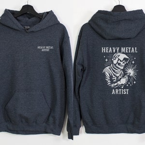May include: A dark gray hooded sweatshirt with the text "Heavy Metal Artist" on the front and a graphic of a skeleton wearing a welding mask and holding a welding torch on the back.