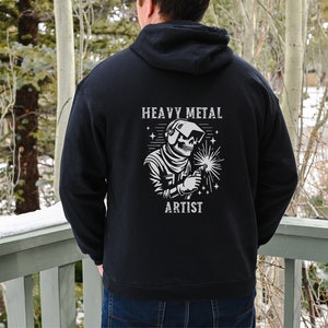 May include: Black hooded sweatshirt with a white graphic of a skeleton welding with the text "Heavy Metal Artist".