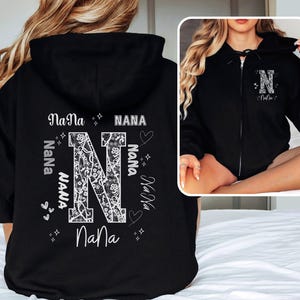 May include: Black zippered hoodie with a white floral letter N and the word "Nana" repeated around it.