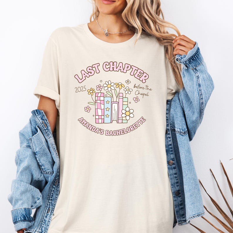 May include: Cream-colored t-shirt with a floral and book graphic. The graphic includes the text "LAST CHAPTER 2025 before the Chapel" and "AMANDA'S BACHELORETTE" in a playful font. The design features flowers and books.