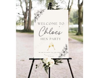 May include: A white welcome sign with black text and floral accents. The sign reads "Welcome to Chloe's Hen Party" with a date of 23.03.25 and the text "We are so happy you are here!"
