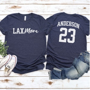 May include: Two navy blue t-shirts. The front of one shirt says "LAX Mom" in white. The back of the other shirt says "Anderson 23" in white.