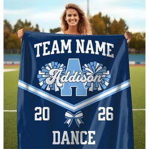 Dance Team Gifts Custom Dance Team Blanket with the team name and dance written at the top and bottom respectively in a varsity font, with the personalized dancer name in the center in between two pom poms, and with a dance team uniform stripe below it, along with a bow below the stripe, and the year arranged on each side.