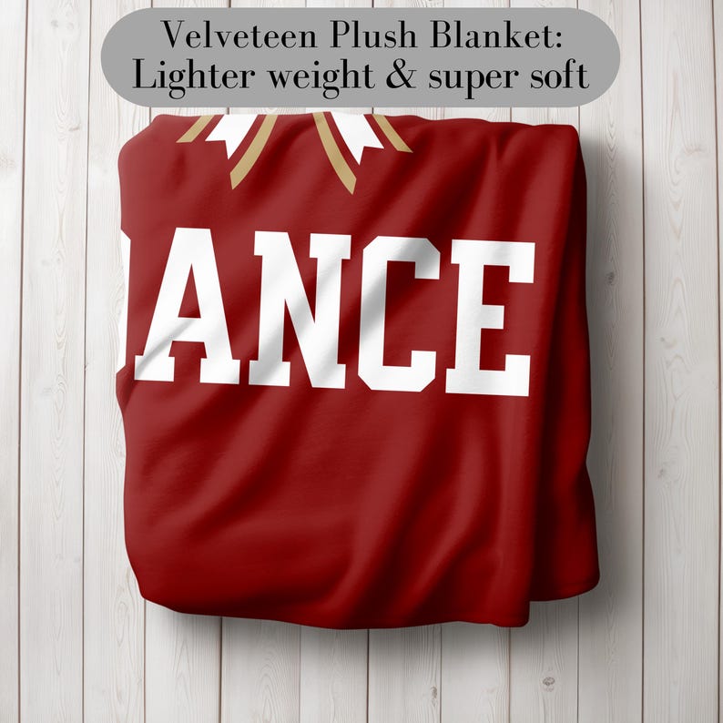 K&ouml;nnte beinhalten: Eine rote Velours-Pl&uuml;schdecke mit dem Wort "ANCE" in gro&szlig;en wei&szlig;en Buchstaben. Die Decke hat goldene Akzente und den Text "Velveteen Plush Blanket: Lighter weight & super soft" in einem grauen Oval.