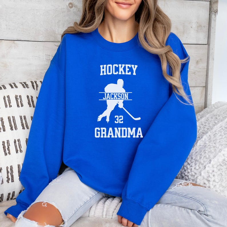 May include: Royal blue sweatshirt with the text "HOCKEY" in white, a silhouette of a hockey player with the text "JACKSON" above and "32 GRANDMA" below.