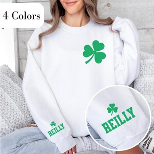 May include: White sweatshirt with a green four-leaf clover design and the text "REILLY" on the sleeve.