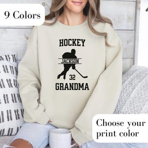 Personalized Hockey Grandma sweatshirt with hockey and grandma written at the top and bottom respectively in varsity font - with a hockey player in the middle with the custom name and optional team number.