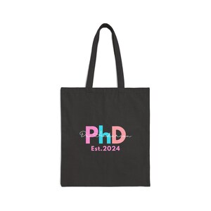 May include: Black tote bag with a pink, blue, and white "PhD" logo and the text "Est. 2024".