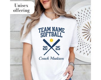 May include: White t-shirt with blue text that says "Team Name Softball" with two crossed baseball bats and a baseball. The numbers 20 and 25 are on the bats. The text "Coach Madison" is below the bats.