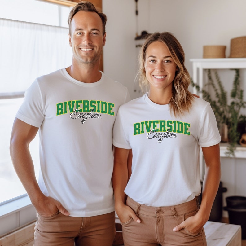 Puede incluir: Dos camisetas blancas con un gr&aacute;fico verde y blanco que dice "Riverside Eagles" en la parte delantera.