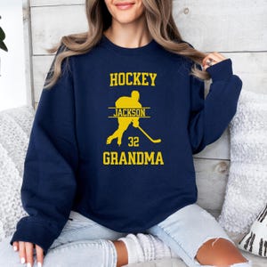 May include: Navy blue sweatshirt with a yellow graphic of a hockey player and the text "HOCKEY JACKSON 32 GRANDMA".