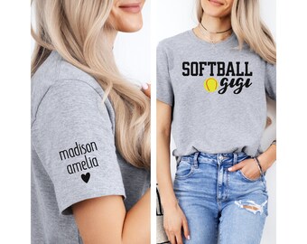 Op de afbeelding: Grijs T-shirt met de tekst "SOFTBALL gigi" en een softball-afbeelding. De linkermouw heeft de tekst "madison amelia" en een klein hartje.