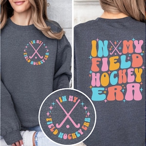 In My Field Hockey Era Sweatshirt with this written in large bubble lettering in alternating muted pastels on the back - with In My Field Hockey Era also written in the front crest in a circle around two crossed field hockey sticks.