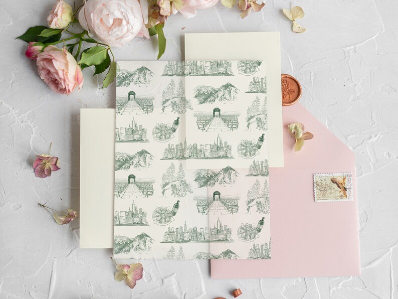 Op de afbeelding: Een set huwelijksuitnodigingen met een roze envelop, een cr&egrave;me envelop en een cr&egrave;me kaart met een groen-wit patroon van stadsgezichten en bergen. De kaart heeft een zegel van was.