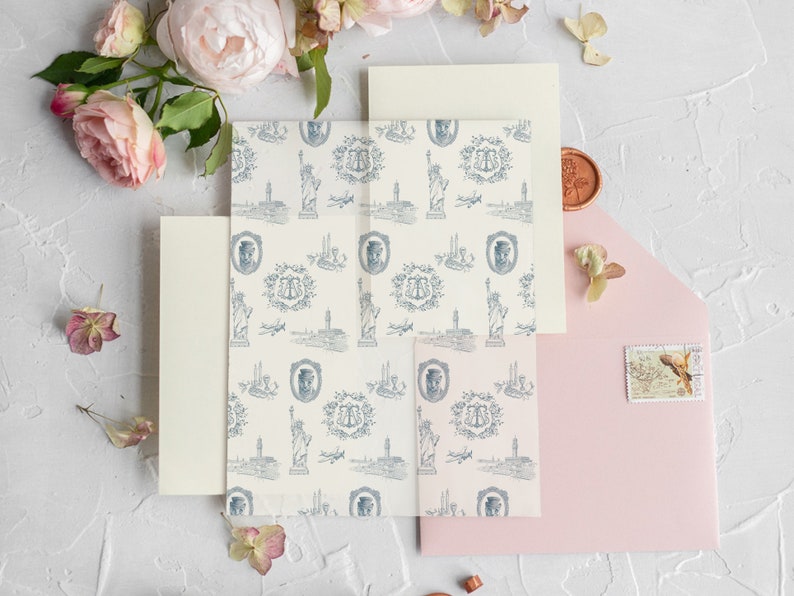 Op de afbeelding: Een set huwelijksuitnodigingen met een lichtroze envelop, een cr&egrave;me envelop en een cr&egrave;me kaart met een blauw-wit patroon van het Vrijheidsbeeld, vliegtuigen en een monogram.