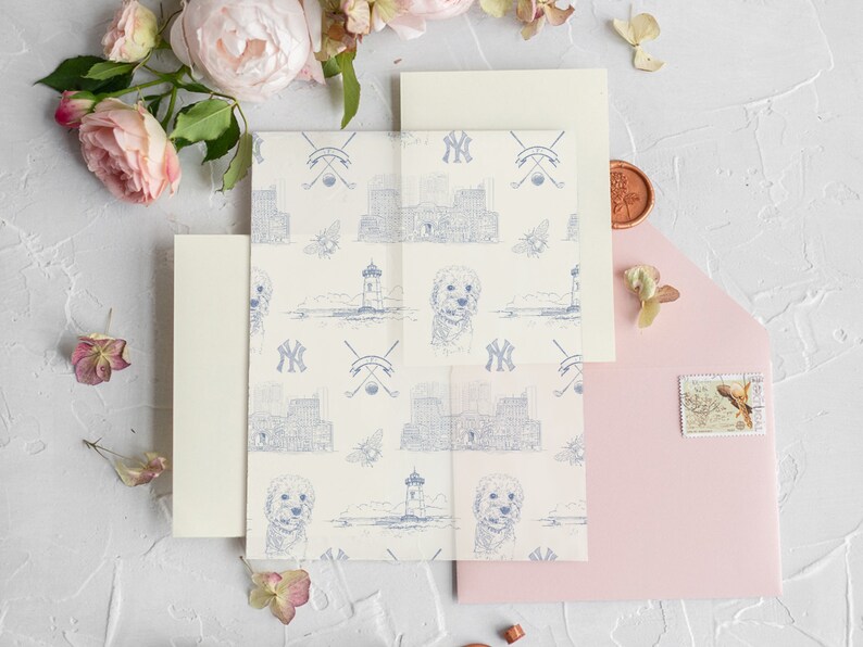 Op de afbeelding: Een set huwelijksuitnodigingen met een witte achtergrond en een blauw-wit patroon. Het patroon bevat een vuurtoren, een hond en de letters "NY". De uitnodigingen liggen op een wit oppervlak met roze en witte bloemen.